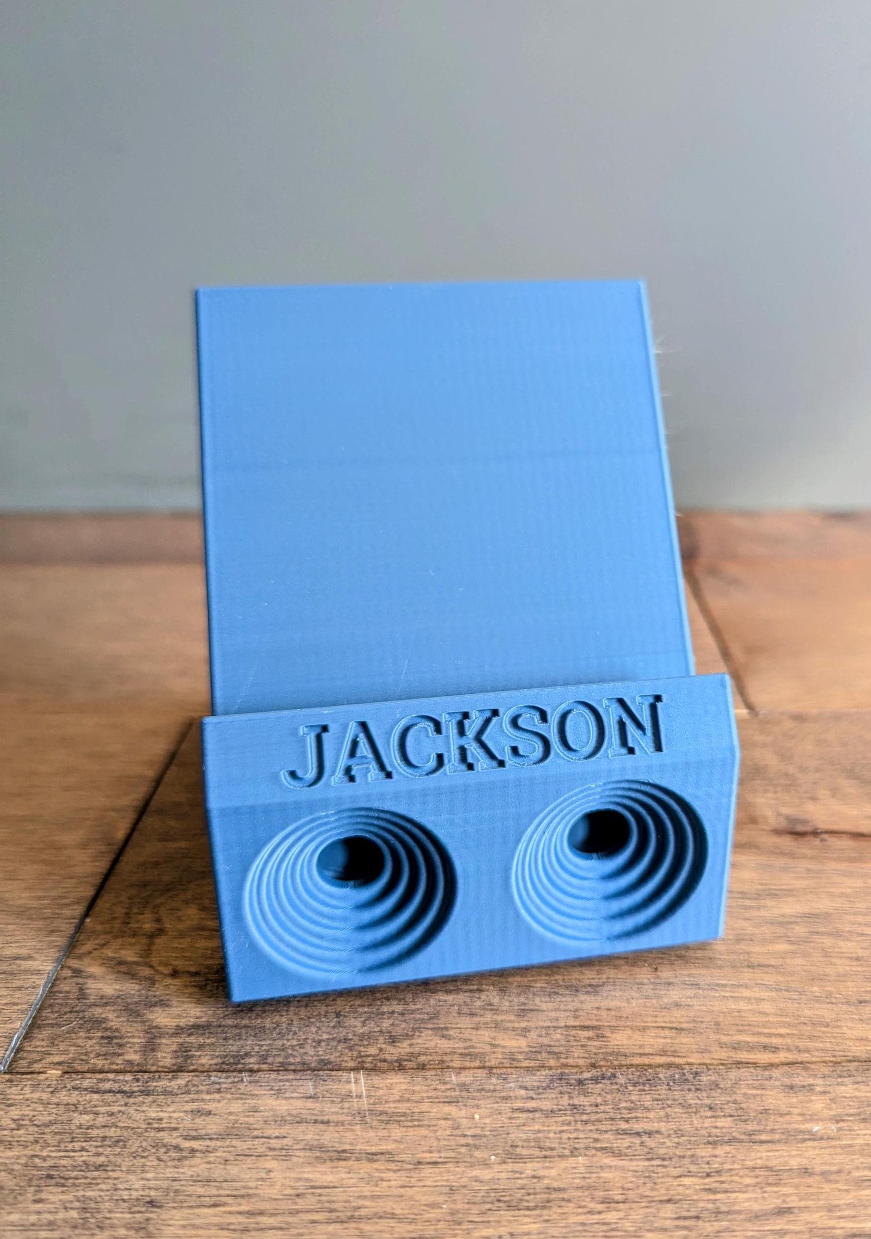 Phone stand with acoustic booster. Back tray ideal for storing air pods or earbuds. Comes in a variety of colors and may be customized for the dimensions of any device. Personalized with name.